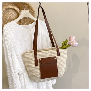 Close-up of woven tote bag with brown leather front pocket and golden rivet details