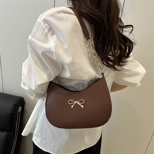 Brown crescent underarm bag with gold bow clasp and chain strap on a model
