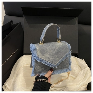 Vue détaillée du sac à main en jean bleu clair avec bords à franges et chaîne dorée en coffret