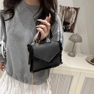 Petit sac à bandoulière noir avec franges et chaîne dorée dans un décor intérieur minimaliste