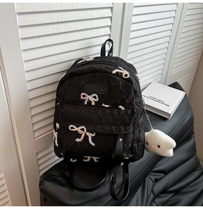 Detail of black quilted backpack with embroidered bows and a plush cloud keychain
