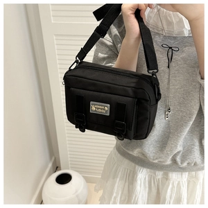 Detail view of a black canvas crossbody bag with decorative leather straps and a fabric label