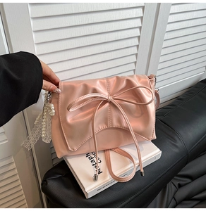 Detail of pink ballet-style bag with large bow, pearl lace charm and pleated leather