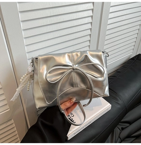 Detail of silver bow shoulder bag with metallic finish and lace pearl charm accessory