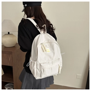 Close-up of a white nylon backpack featuring a yellow smiley patch and woven zipper pullers