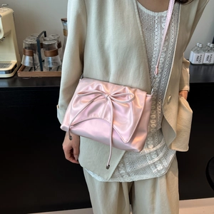 Pink ballet-style satin crossbody bag with large bow detail and glossy finish
