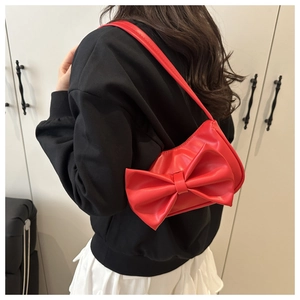 Detailed view of a stylish red bow shoulder bag worn on the shoulder with a leather strap