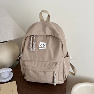 Minimalist khaki college backpack with smiley patch and side drawstrings on wooden desk