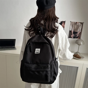 Minimalist black nylon backpack with smiley face patch shown on model back