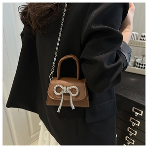 Detailed view of caramel brown mini handbag with sparkling rhinestone bow on black blazer