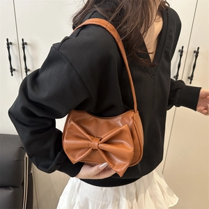 Caramel brown underarm bag with a large bow detail held by a model in casual attire
