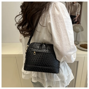 Detail of a black woven shell bag with gold hardware worn over a white blouse