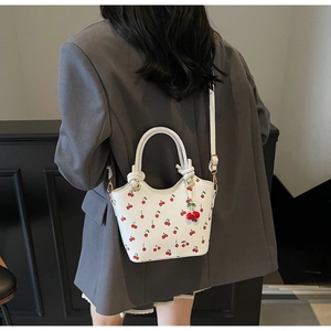 Close-up of white bucket bag featuring cherry prints and red cherry charm detail