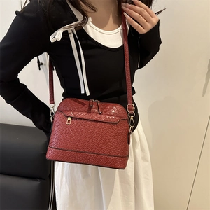 Red crocodile texture shell bag with gold hardware worn by a model in a stylish outfit