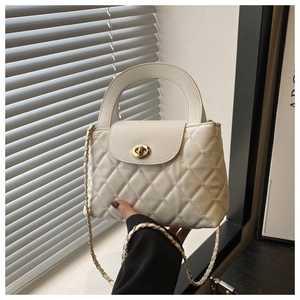 Detail of white quilted handbag featuring a gold turn-lock closure and leather chain strap
