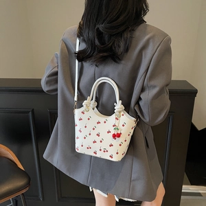 Retro white bucket bag with cherry print and charm carried by a model in a grey suit