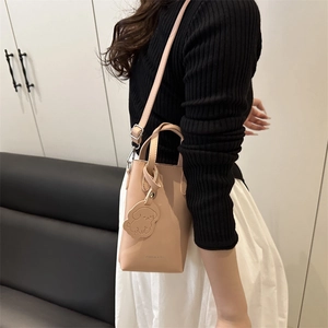 Elegante borsa a secchiello beige con ciondolo a cane, mostrata con tracolla