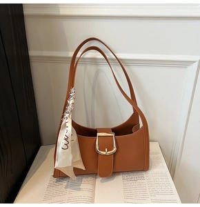 Détail d'un sac demi-lune marron avec boucle dorée et foulard en soie à imprimé floral