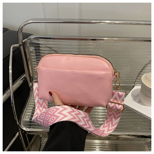 Detail of pink PU leather camera bag with wide geometric knit shoulder strap and gold hardware