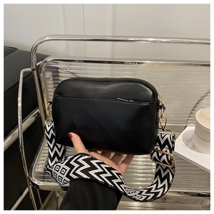 Detail of black crossbody bag featuring a wide geometric pattern strap and gold zipper