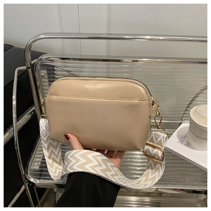 Detail view of beige camera bag with patterned wide strap on a modern acrylic shelf