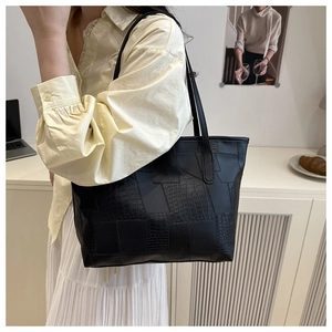 Detail of black tote bag showing crocodile pattern texture and smooth faux leather finish