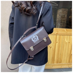 Detail of dark brown leather messenger bag with embroidered crest and metal locks