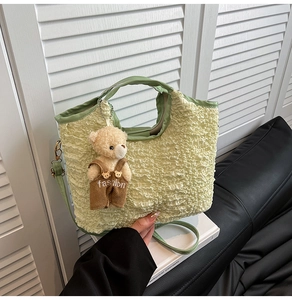 Detail view of light green pleated bucket bag with a cute plush bear charm on white desk