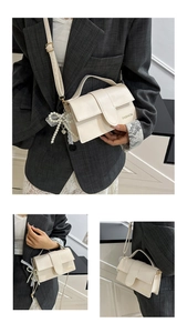 Detail of cream leather shoulder bag with a pearl lace bow charm and gold fashion logo