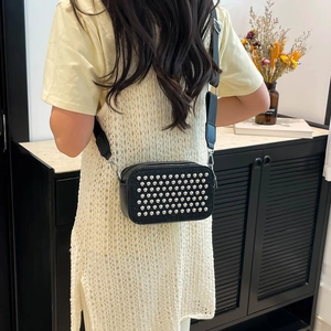 Stylish black crossbody camera bag with silver rivets and wide strap worn by a model