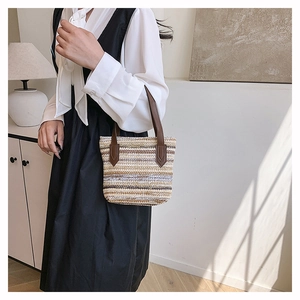 Detail shot of the mixed-color woven straw bag with dark brown leather handles on a model