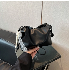 Detail of black pleated bucket bag featuring pearl and lace pendant on side