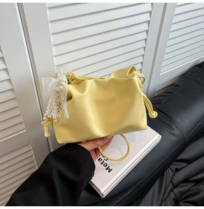 Detail of yellow pleated handbag featuring lace bow, pearl charm, and metal ring handle