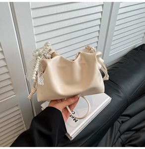 Detail of creamy white cloud bag with pearl bow and lace trim on a white book