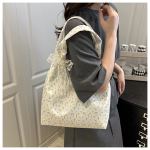 Floral canvas tote bag with lace bow detail shown on shoulder for size reference