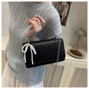 Close-up of black woven leather handbag with pearl bow charm and silver metal handle