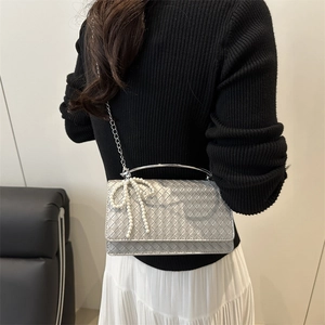 Silver woven handbag with pearl bow and metal handle shown on a model in white skirt