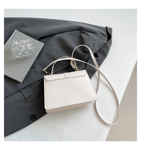 Detail of a minimalist beige leather crossbody bag with a gold metal buckle for women
