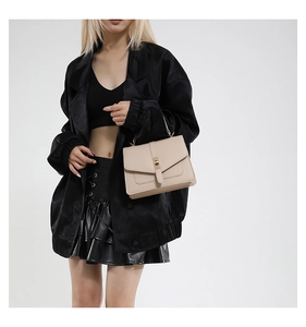 Close-up of apricot leather crossbody bag with gold metal lock on a black outfit