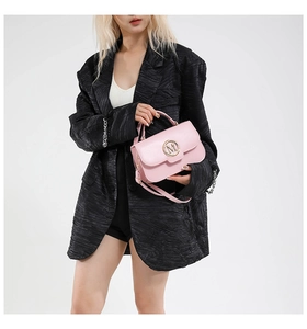Close-up of pink leather handbag with gold M buckle on black blazer background