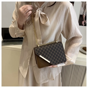 Detail of vintage patterned flap crossbody bag with gold chain strap on office desk