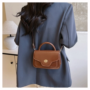 Detail of vintage brown leather saddle bag featuring a round golden twist lock and top handle
