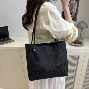 Modern black tote bag with butterfly embroidery and braided shoulder strap shown on model