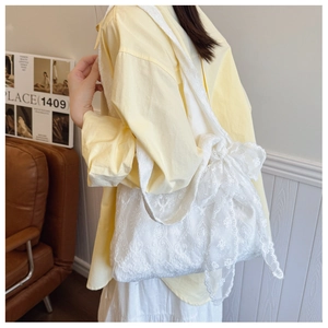 Detail of white lace tote bag featuring intricate floral embroidery and a large side bow