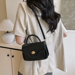 Vintage black faux leather saddle bag with gold metal clasp shown on a shoulder