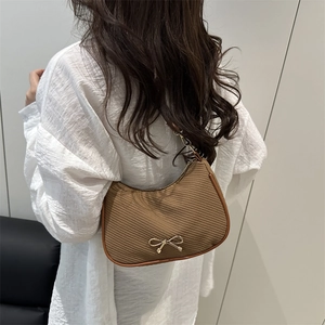 Brown crescent shoulder bag with golden bow ornament shown on female model back