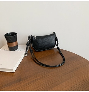 Close-up of black lychee grain leather crescent bag with decorative knotted strap detail