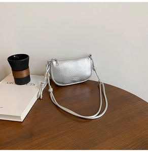 Detail of silver crossbody bag featuring litchi texture finish and knotted strap
