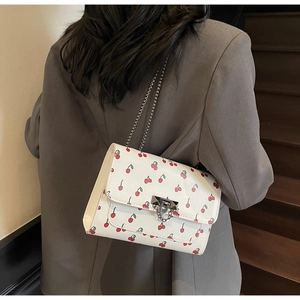 Détail du sac bandoulière blanc avec imprimé cerise et bandoulière en chaîne argent