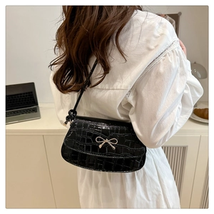 Detail of black faux leather bag with crocodile texture and silver metal bow on shoulder strap